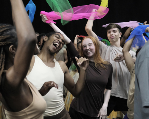 young people mixed genders and races dancing together with big smiling faced waving brightly colour scarfs. 