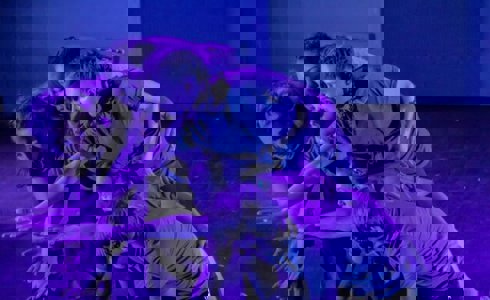 six young dancers all huddled together reaching for the same spot in the bottom left on the screen with blue lighting