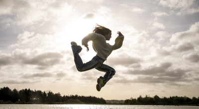 white female dancer jumping in the air in a running shape in front of golden clouded sky wearing casual clothes