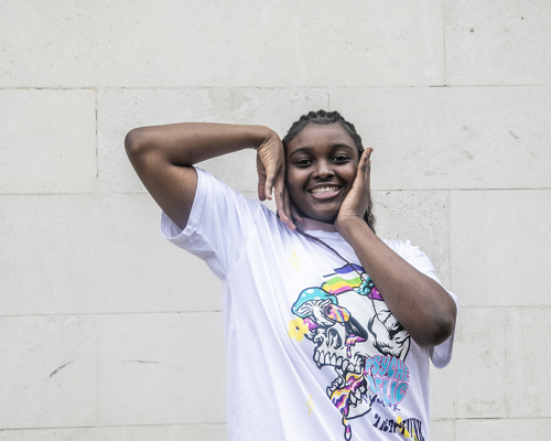 young global majority female dancer with long black braids. Arms framing the face. Wearing white graphic tshirt