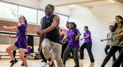 black male dancer  teaching a group of young people to dance. all in a running man position wearing athletic clothing in a dance studio. 