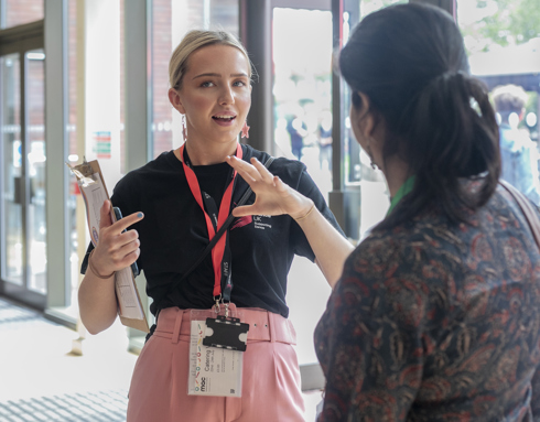 White female with tied back blonde hair One Dance UK Staff member gesturing to someone in discussion in front of glass doors