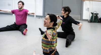 global majority female dancer teaching community group. Arm stretched open sitting with legs wise on the floor in the dance studio. 