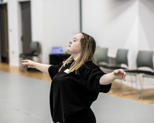 White blonde female down syndrome dancer with arms spread out head up wearing black in a dance studio 